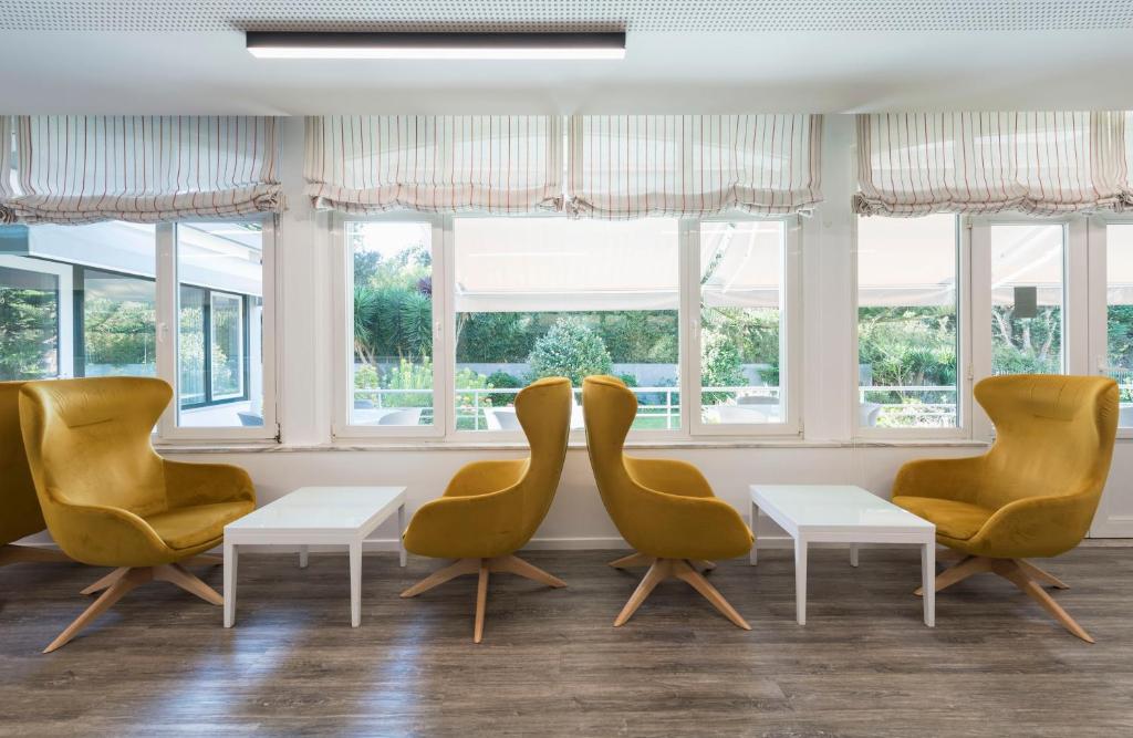 una sala de espera con sillas amarillas, mesas y ventanas en Varzinn Hotel, en Póvoa de Varzim