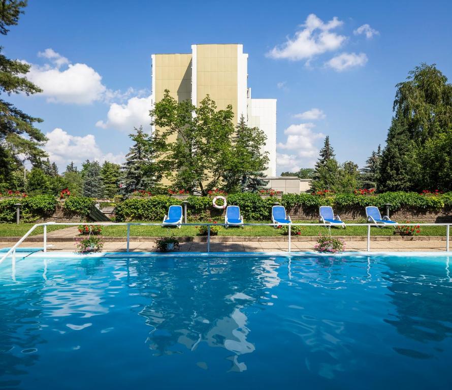 a pool with chairs and a building in the background at Ensana Thermal Hévíz in Hévíz