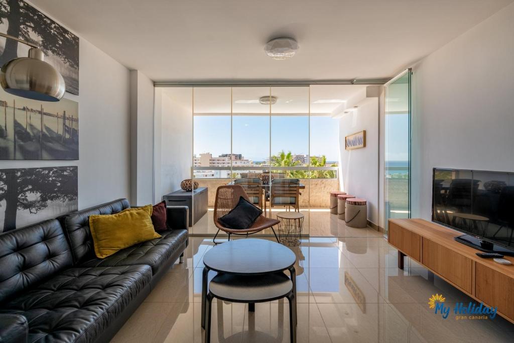 a living room with a black leather couch and a television at Esther's Sea View in Playa del Ingles