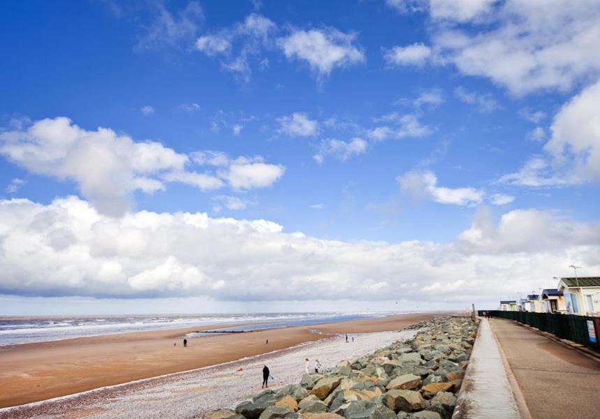 a beach with people walking on the sand and rocks at Golden Sands Holiday Park in Kinmel Bay