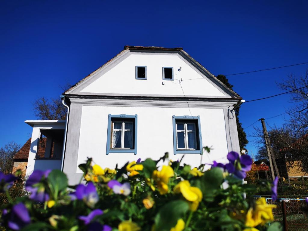 a white house with blue windows and purple flowers at Őrség Kincse Udvarház in Hegyhátszentjakab