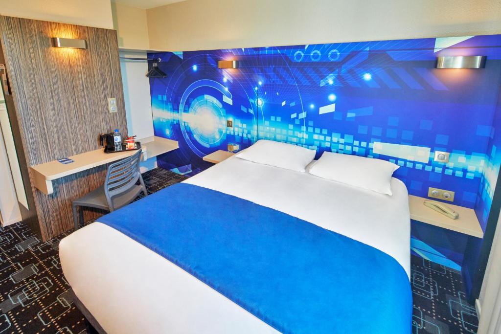 um quarto com uma cama azul e branca e uma secretária em Kyriad Poitiers Jules Verne Site du Futuroscope em Chasseneuil-du-Poitou