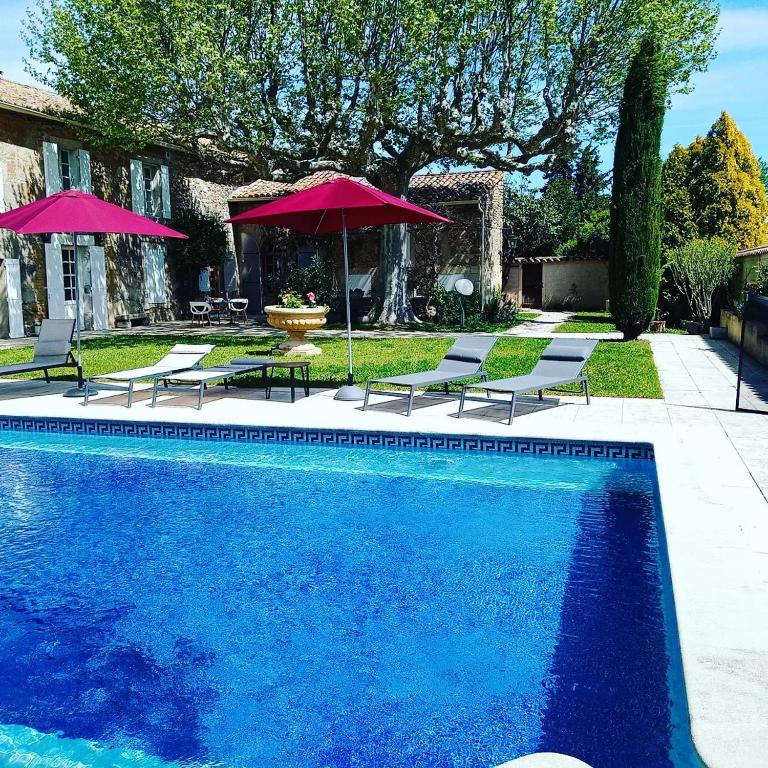 a pool with chairs and umbrellas next to a house at LE MAS DES FLANERAIES in Althen-des-Paluds