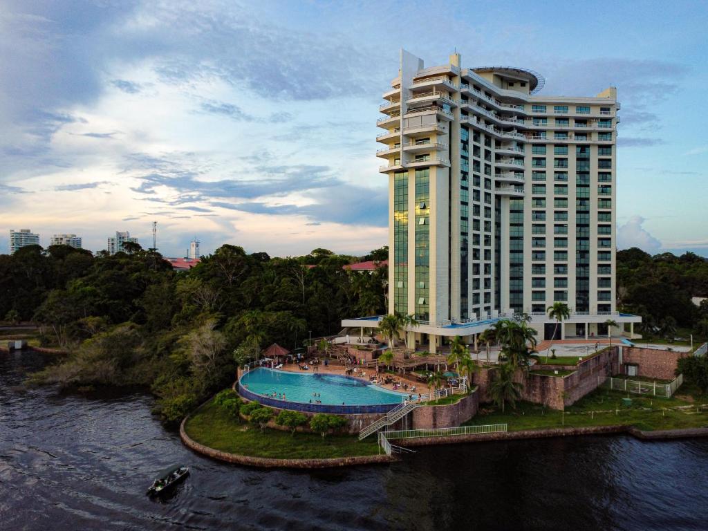 a large building with a swimming pool next to a river at Tropical Executive Hotel in Manaus