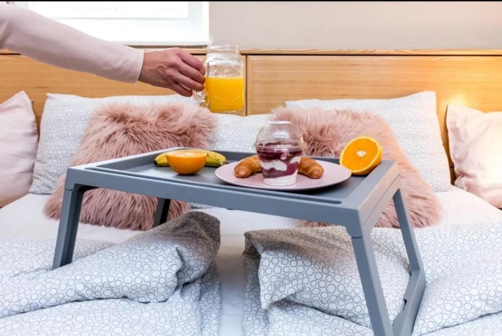 a tray of food and orange juice on a bed at Center Firefly Danube Apartment in Novi Sad