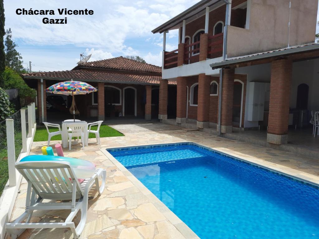einen Pool mit Stühlen und einem Sonnenschirm neben einem Haus in der Unterkunft Chácara Vicente Gazzi in Socorro