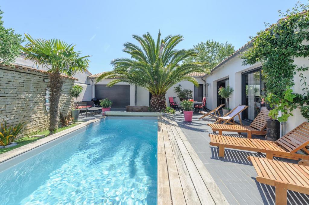 una piscina con sillas y palmeras en un patio trasero en Villa Lizelya, en La Couarde-sur-Mer