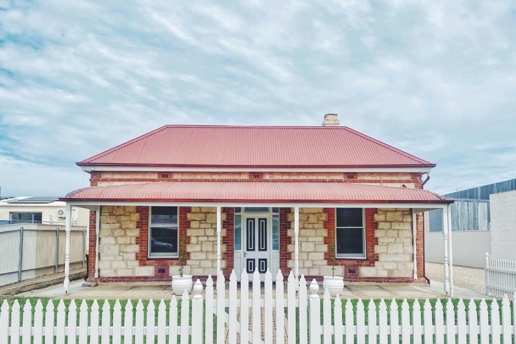 a small brick house with a red roof behind a white fence at The Central Cottage - Port Lincoln in Port Lincoln