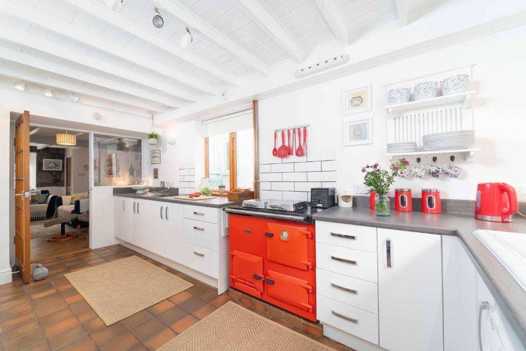 a kitchen with white counters and red cabinets at Curlew Cottage in Uny Lelant