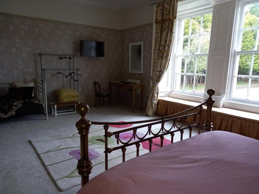 a bedroom with a bed and a desk and windows at Gardenvale Manor House B&B in Stranocum