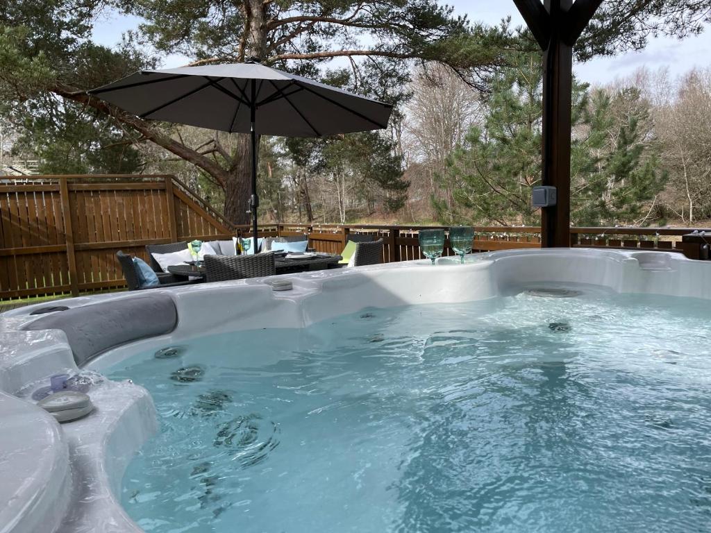 a hot tub with an umbrella in a backyard at Luxury Riverside Lodge, Blair Atholl in Pitlochry