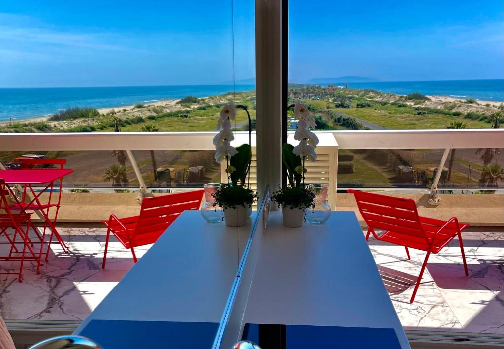 - une table bleue sur un balcon avec des chaises rouges et l'océan dans l'établissement Caraïbes Heliopolis naturiste, au Cap d'Agde