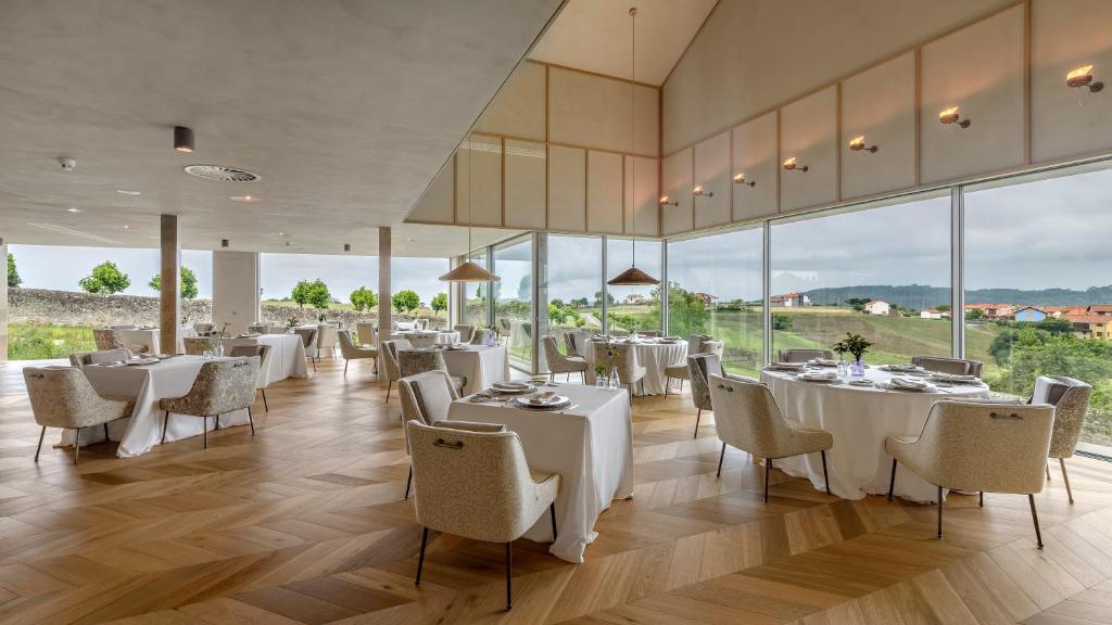 Un restaurante con mesas y sillas blancas y grandes ventanales. en CoolRooms Palacio de Luces, en Luces