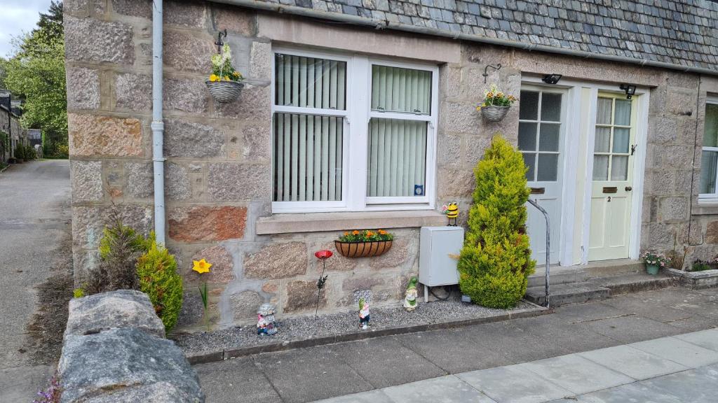 a stone house with a door and flowers in front of it at Deeside Holiday Cottages in Dinnet