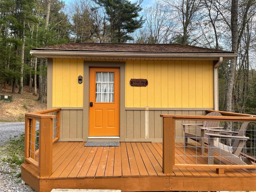 ein kleines gelbes Haus mit einer orangefarbenen Tür auf einer Terrasse in der Unterkunft Country Cottage at Camp Creek Cabins in Spanishburg