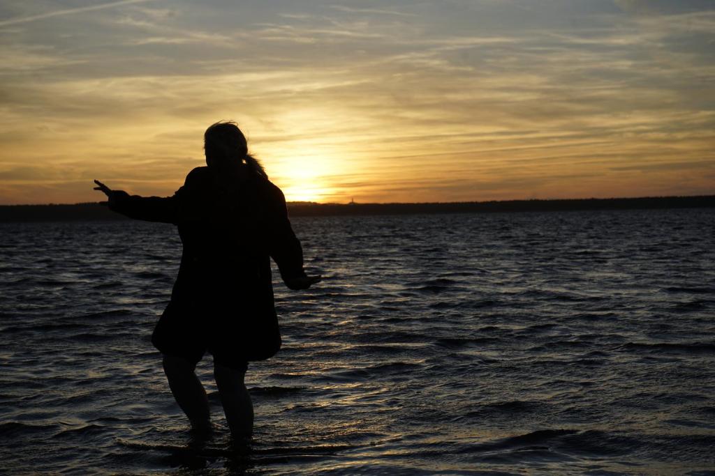 a woman standing in the water with the sunset in the background at Nordlicht II in Trent