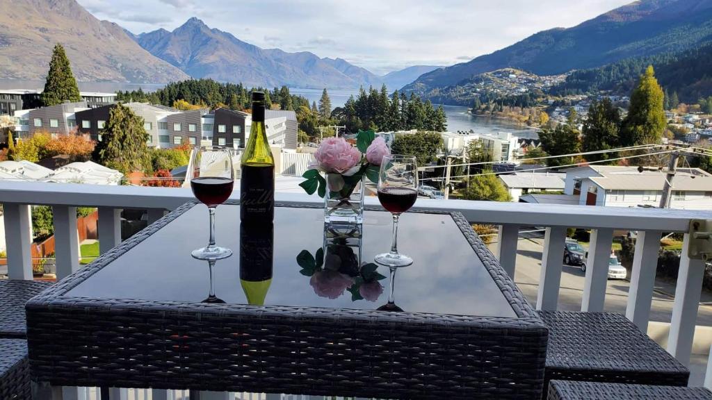a table with two glasses of wine and flowers on a balcony at Central Lakeview Apartment with amazing rooftop 镇上湖景三室套房 in Queenstown
