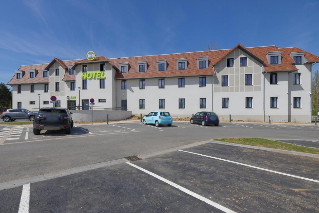 ein großes weißes Gebäude mit Autos auf einem Parkplatz in der Unterkunft B&B HOTEL Le Touquet in Cucq