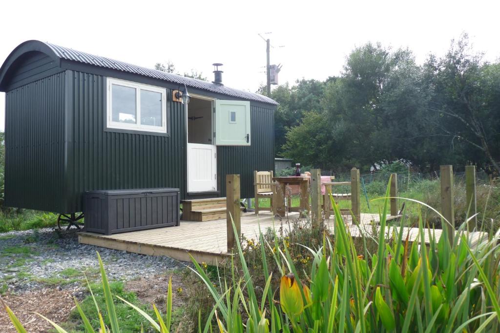 a green tiny house sitting on a wooden deck at Shepherds Hut on Cornish Smallholding in Penzance