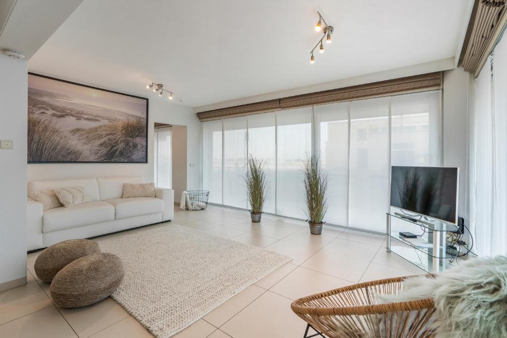 uma sala de estar com um sofá branco e uma televisão em Gelijkvloers zeedijk appartement - lichtrijk en modern em Blankenberge