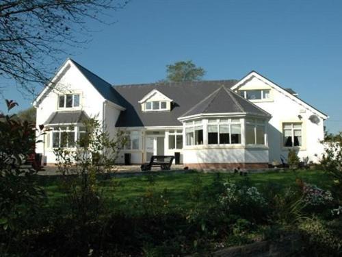 een groot wit huis met een bankje ervoor bij Hazelwood House in Bridgend