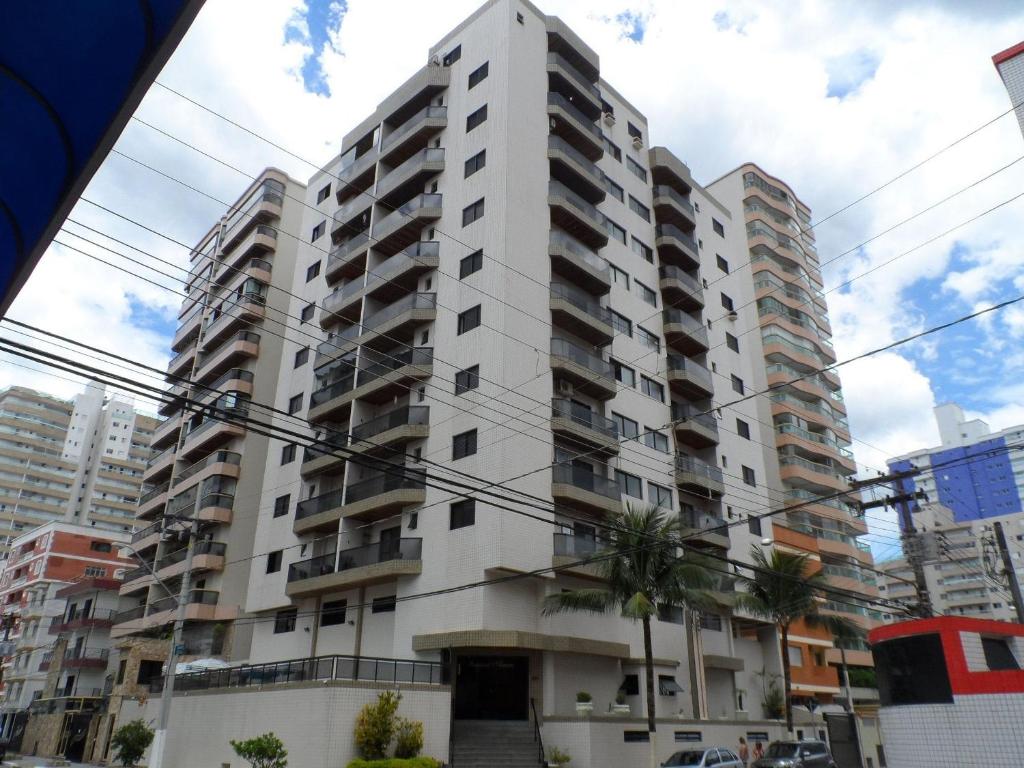 Un edificio alto y blanco con palmeras delante. en T004 - Apto na Tupi com sacada, garagem e ótima localização, en Samaritá
