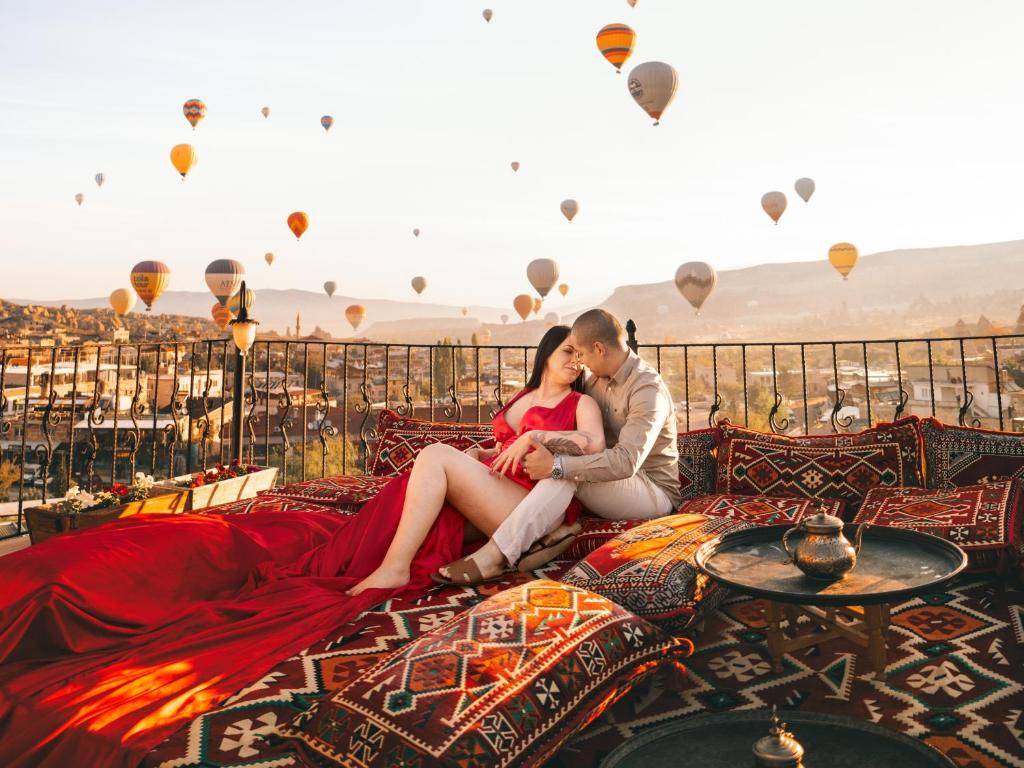 una pareja sentada en una cama viendo globos de aire caliente en APEX CAVE HOTEL en Goreme