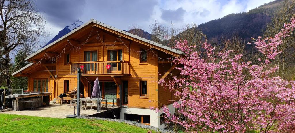 a wooden house with a tree with pink flowers at Chalet les Vagnys - Lac des Vernays in La Rivière-Enverse