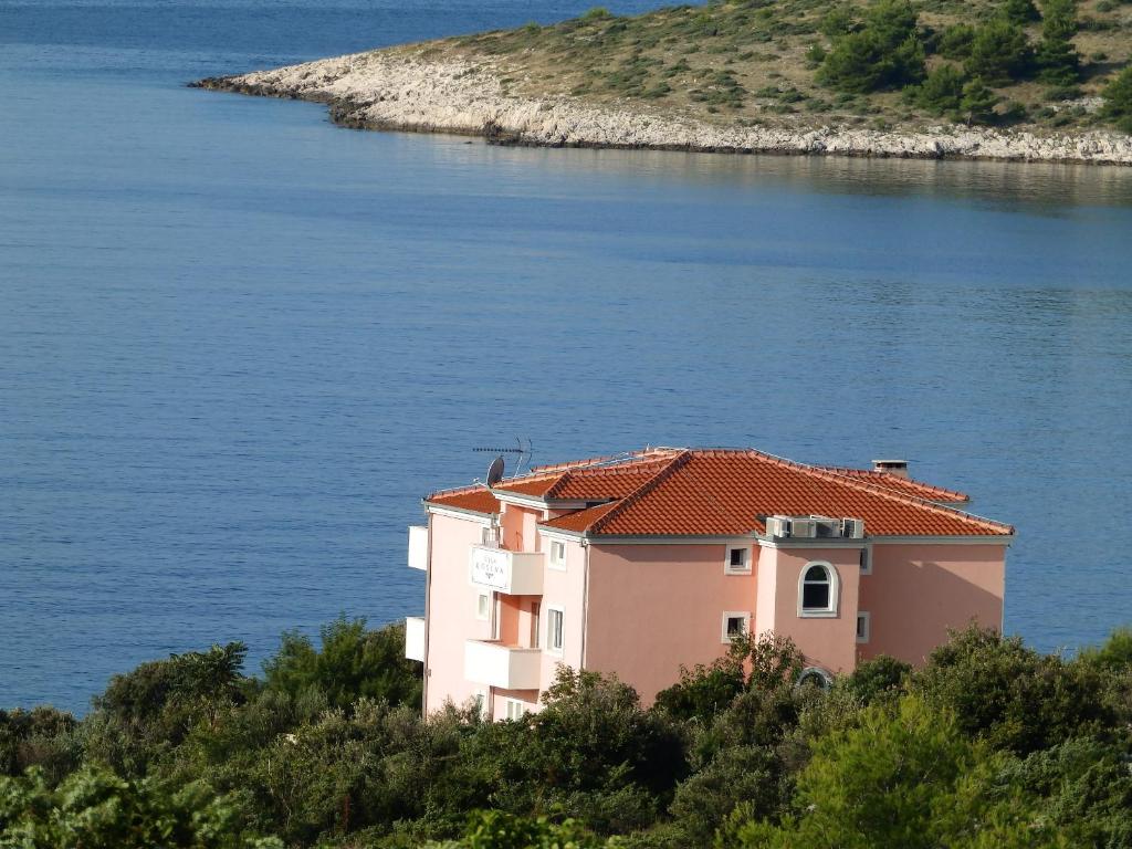 a pink house on a hill next to the water at Apartments Villa Rosina in Rogoznica