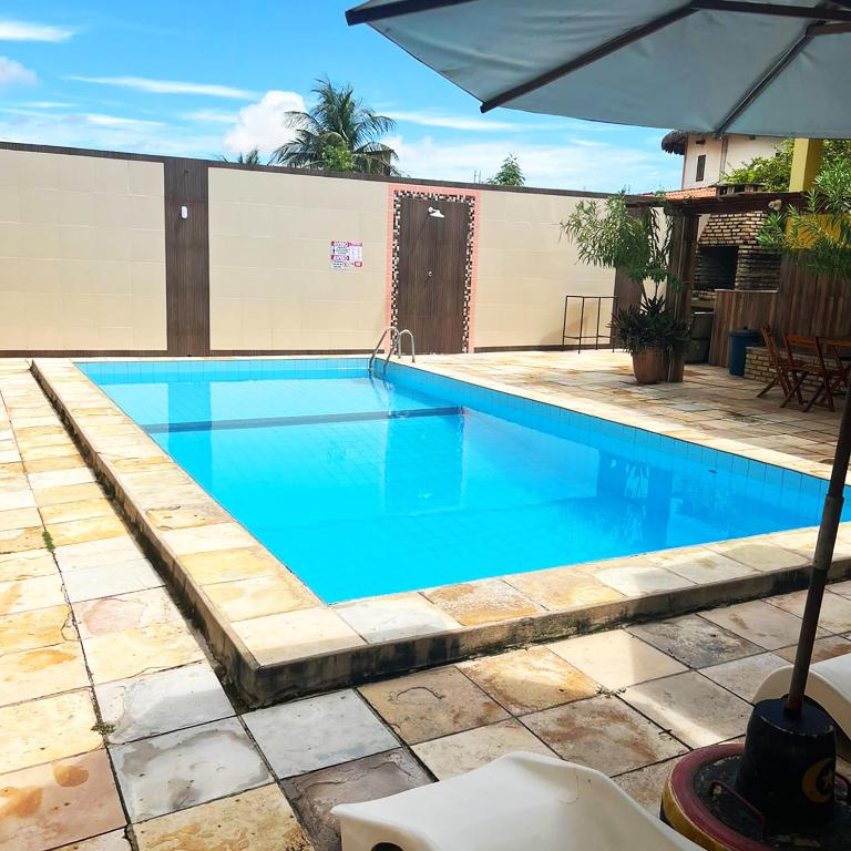 a large blue swimming pool with an umbrella at Pousada Chalet La Pink in Canoa Quebrada