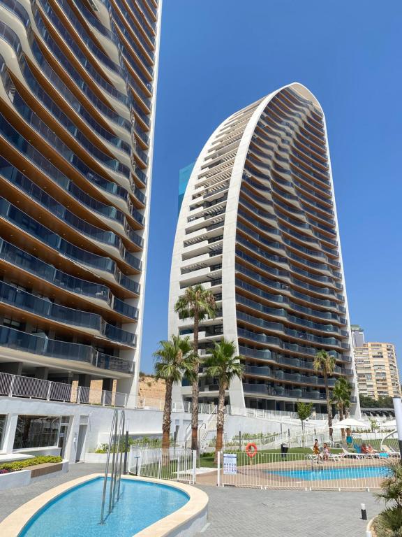 two tall buildings with palm trees and a swimming pool at SUNSET WAVES blue sky apartment in Benidorm