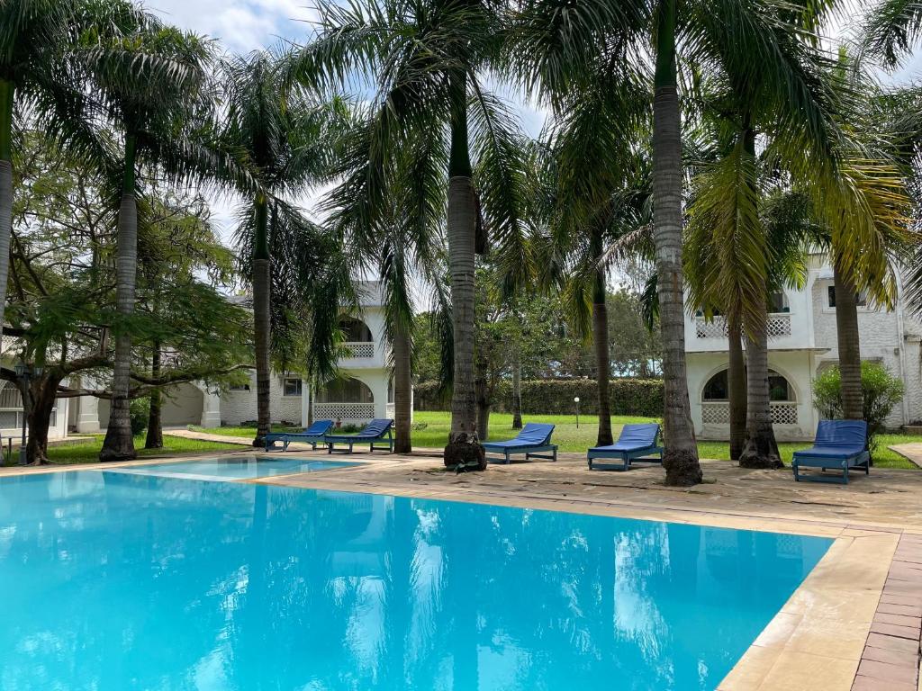 a pool with palm trees and blue lounge chairs at Royal Palms Apartment A4 in Mombasa