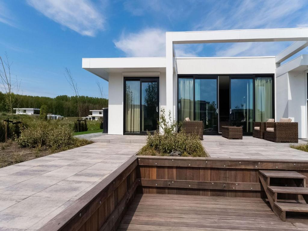 une maison blanche avec une terrasse en bois et du verre dans l'établissement Swanky villa in Zeewolde with garden, à Zeewolde