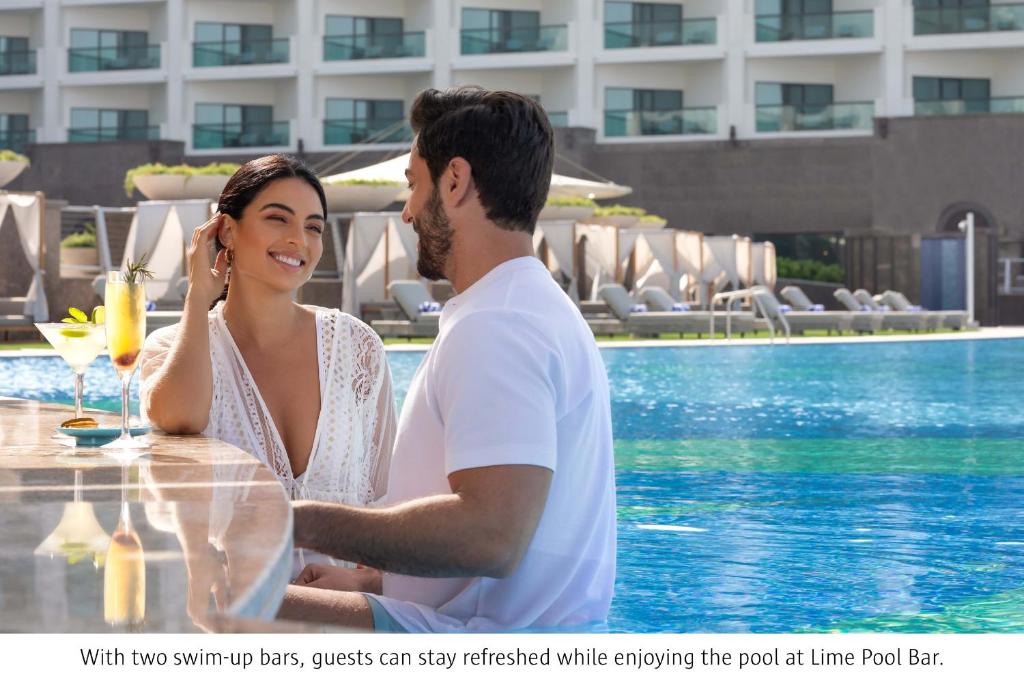 a man and a woman sitting at a table by a pool at Taj Exotica Resort & Spa, The Palm, Dubai in Dubai