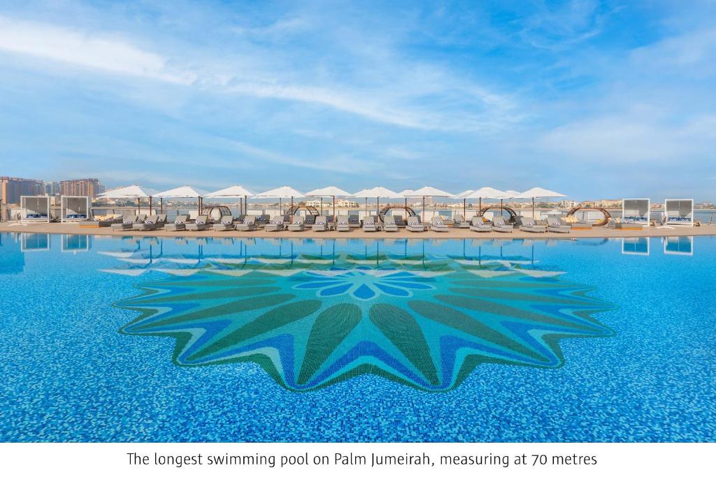 a swimming pool with chairs and umbrellas on a beach at Taj Exotica Resort & Spa, The Palm, Dubai in Dubai