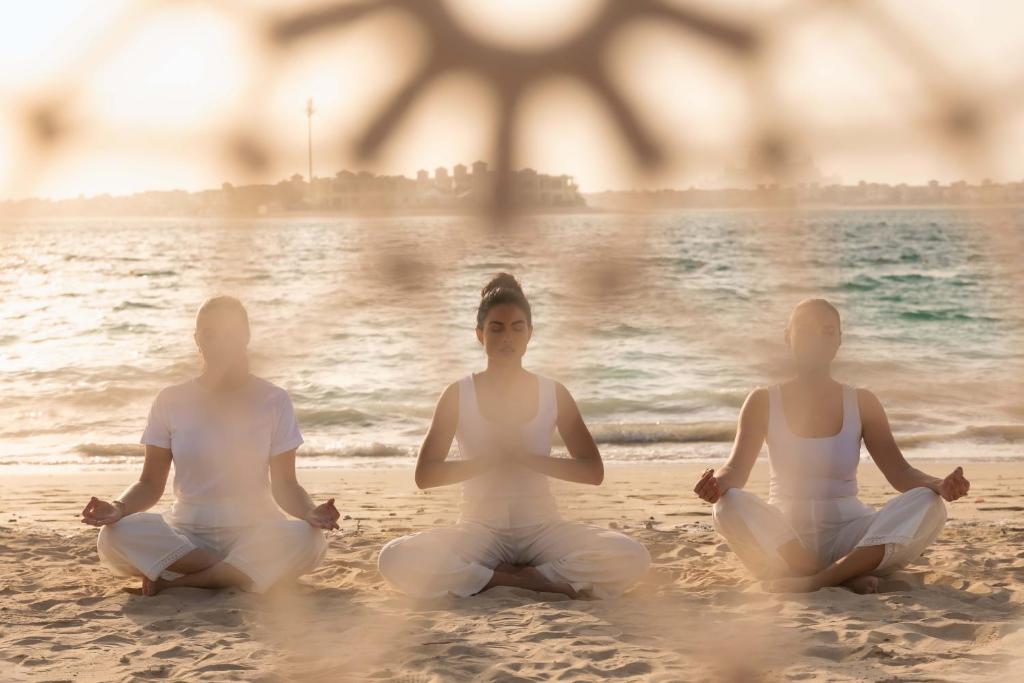 three women sitting in meditation on the beach at Taj Exotica Resort & Spa, The Palm, Dubai in Dubai