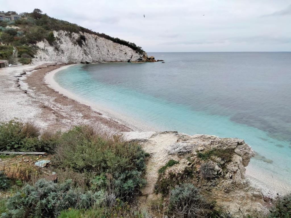 a beach with blue water next to a cliff at Padullella, mare e sole!! in Portoferraio
