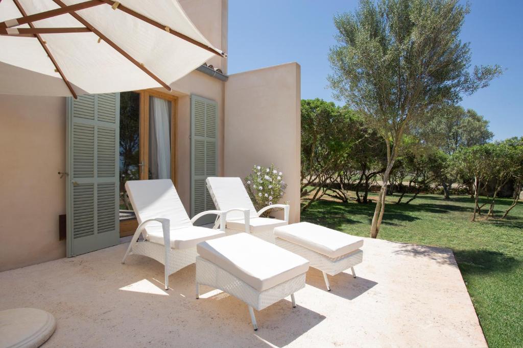 a patio with white chairs and an umbrella at Fontsanta Hotel Thermal & Spa - Adults Only in Colònia de Sant Jordi