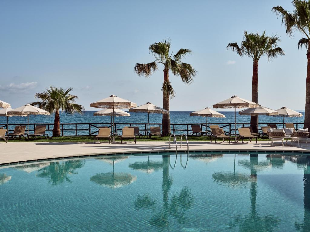 una piscina con sedie, ombrelloni e oceano di Windmill Bay Hotel ad Argásion