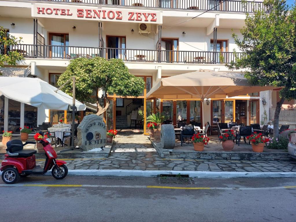 un scooter estacionado frente a un hotel con mesas y sombrillas en Xenios Zeus en Ouranoupoli
