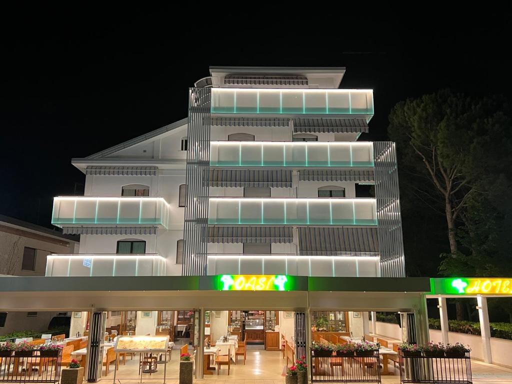 un edificio blanco alto con un restaurante frente a él en Hotel Oasi, en Lignano Sabbiadoro