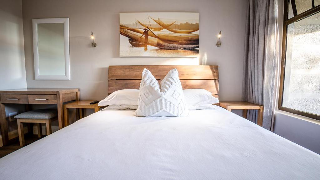 a bedroom with a large white bed and a desk at Modern self-catering apartment in a secure estate in Plettenberg Bay