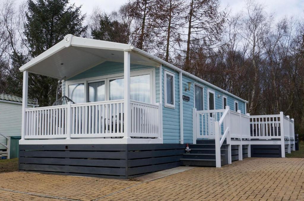 a blue tiny house with a white porch and a porch at Silver Birch Retreat - Percy Woods Country Retreat With 18 HOLE FREE GOLF in Alnwick