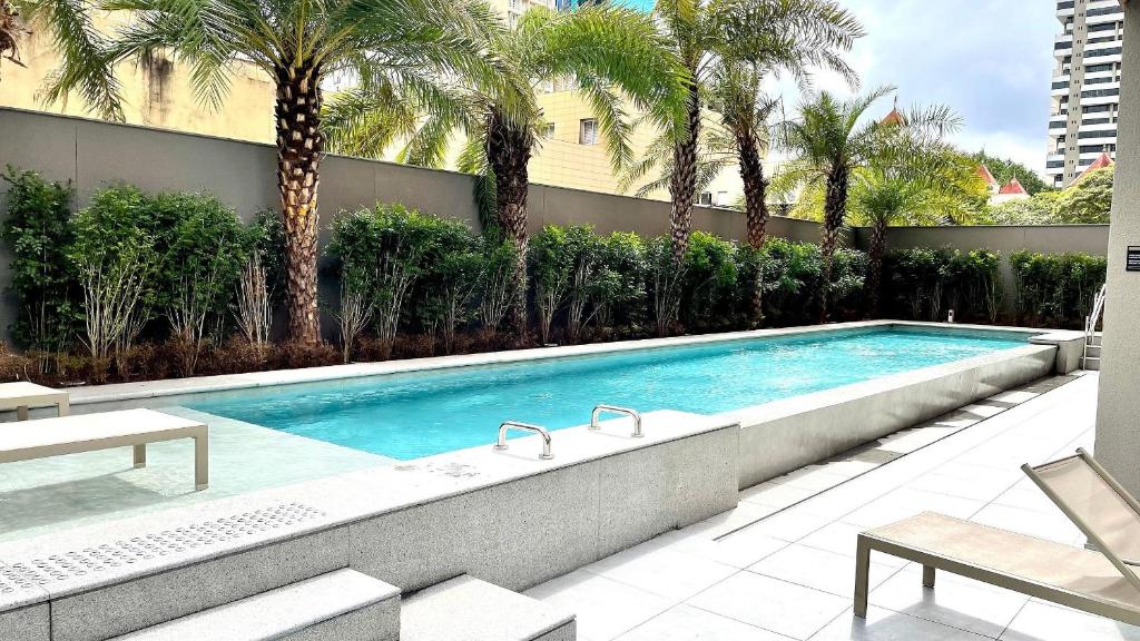 a swimming pool with palm trees in front of a building at Haus Stay . Luxo . Vitralli Moema in Sao Paulo
