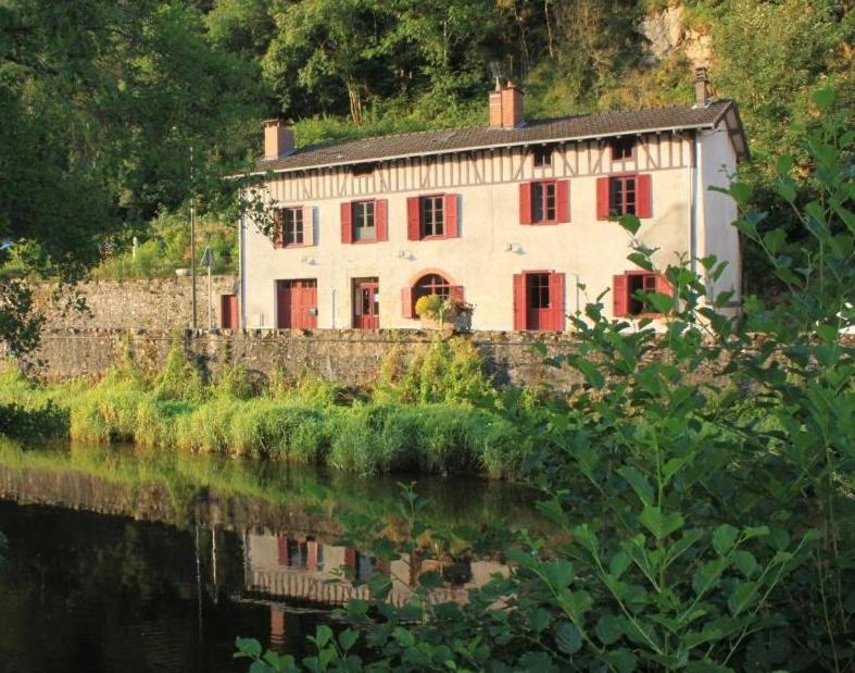 una casa con porte rosse è vicino a un fiume di Chambres d'hôtes Le Veilleur de Noblat a Saint-Léonard-de-Noblat