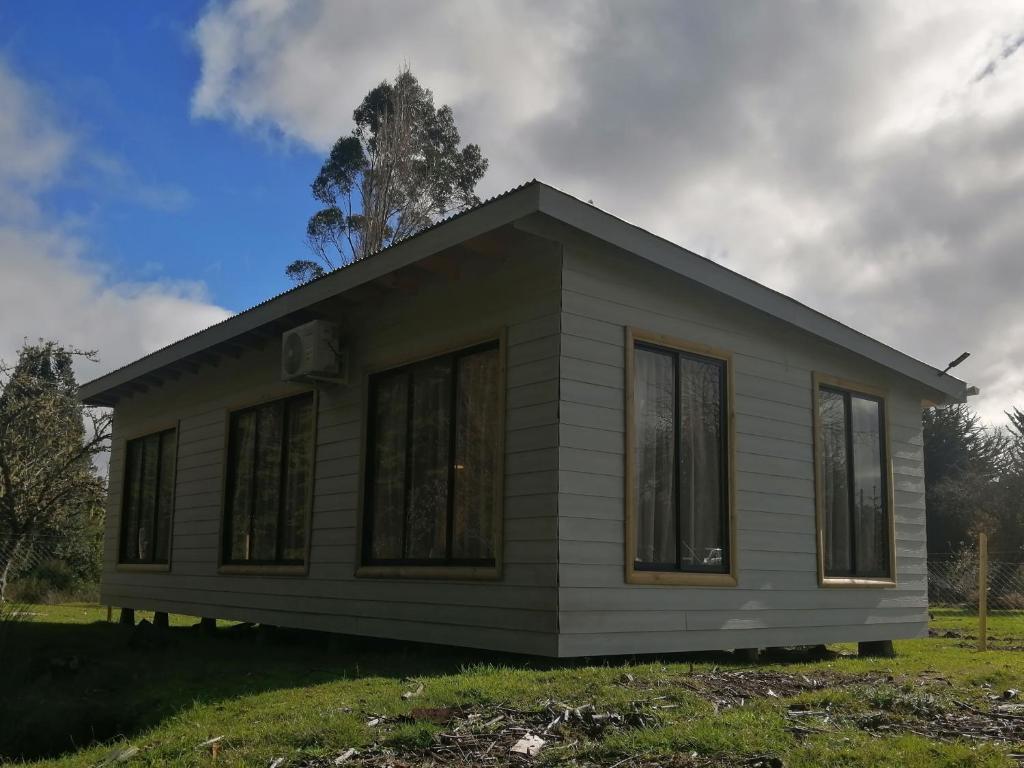 a small white house with windows on a field at Cabañas camelia in Puelo