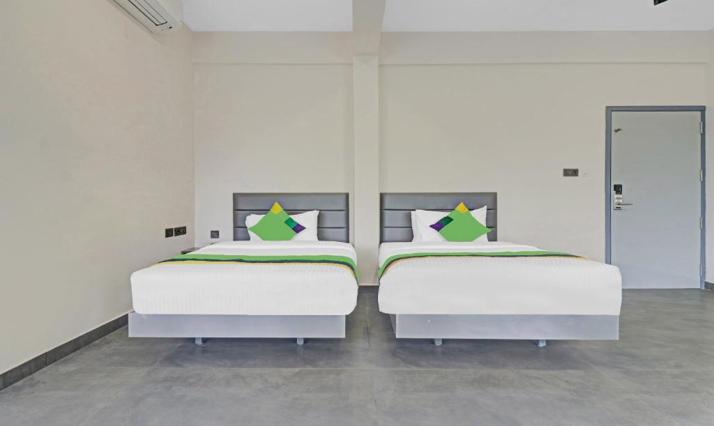 two beds in a room with white walls and green pillows at Treebo Grand Vistara Airport Suites in Cochin
