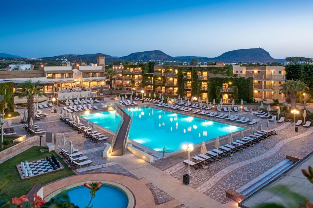 a large swimming pool with lounge chairs and buildings at Bella Beach Hotel in Hersonissos