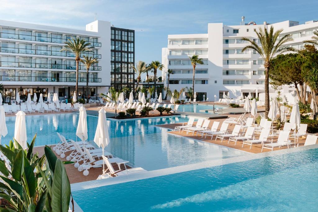 Una piscina con tumbonas y un hotel. en AluaSoul Ibiza - Adults only, en Es Canar