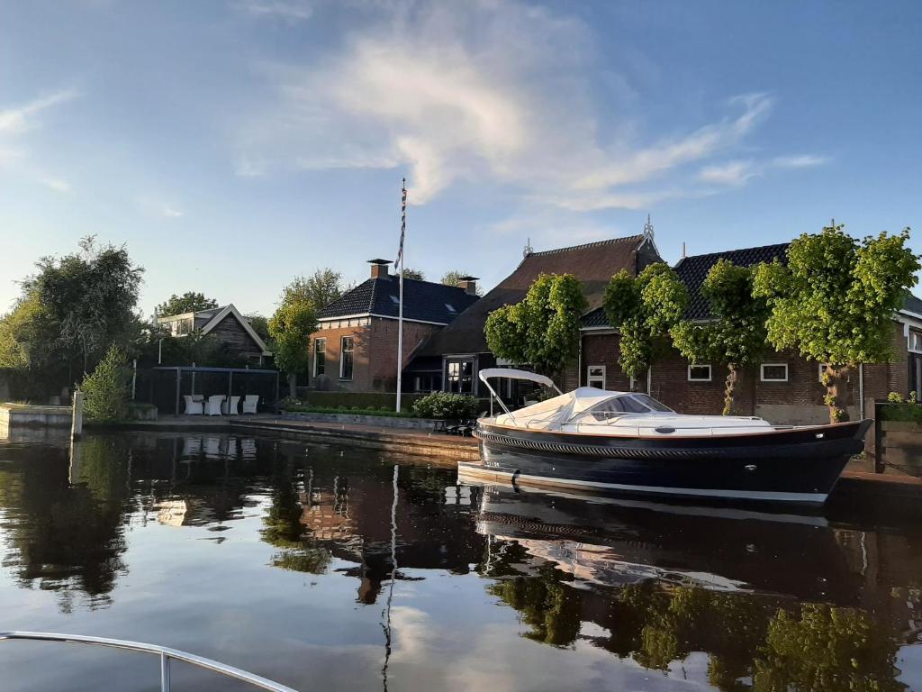 a boat is docked on the water in front of houses at PUUR Eastermar - monumentaal, authentiek en luxe koetshuis aan open vaarwater met jacuzzi en sauna in Oostermeer